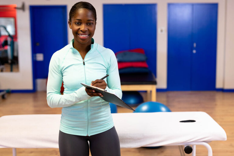 Happy,Female,Trainer,Looking,At,Camera,While,Writing,On,Clipboard